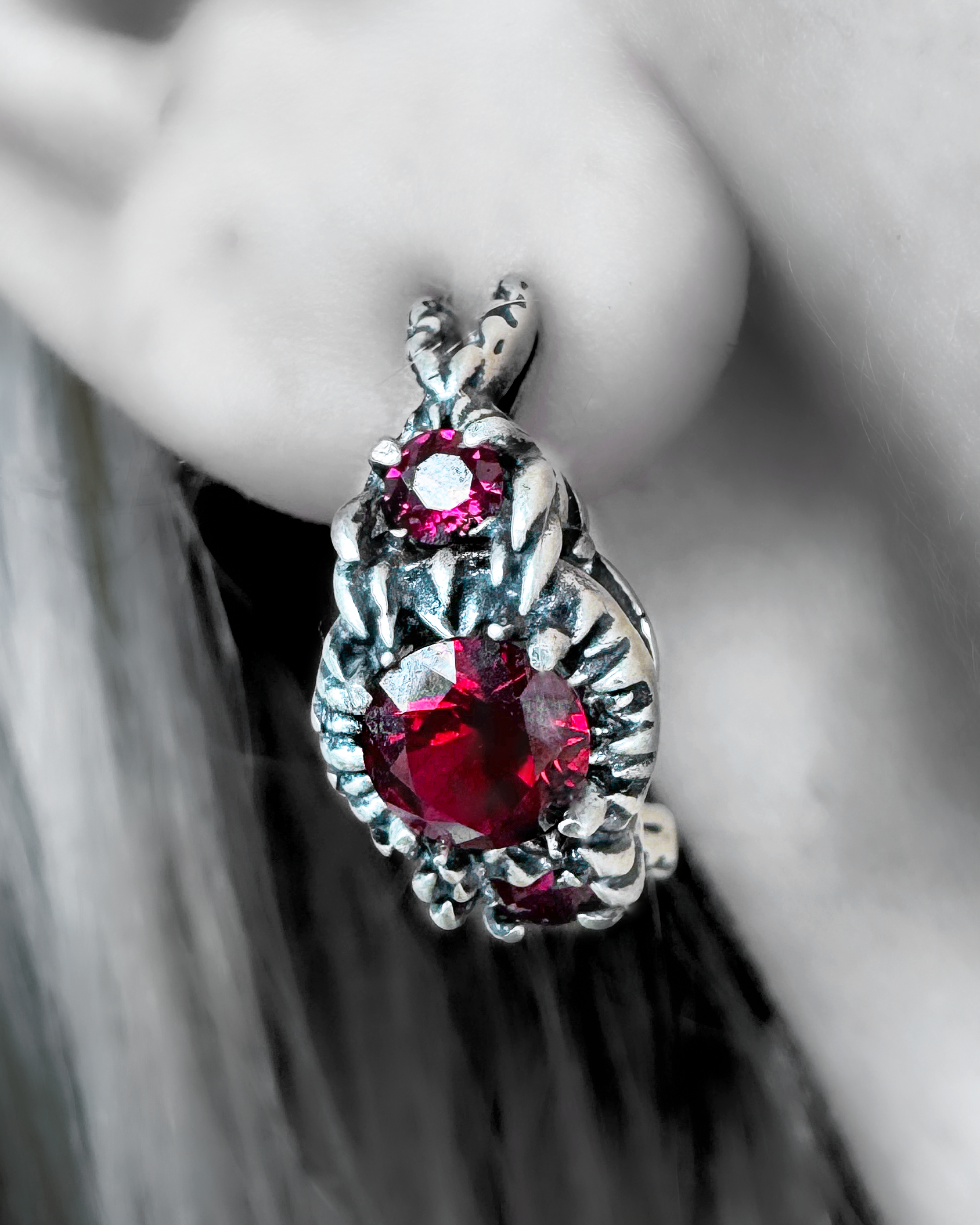 A pair of silver earrings with claw like prongs holding a ruby on a female’s ear.