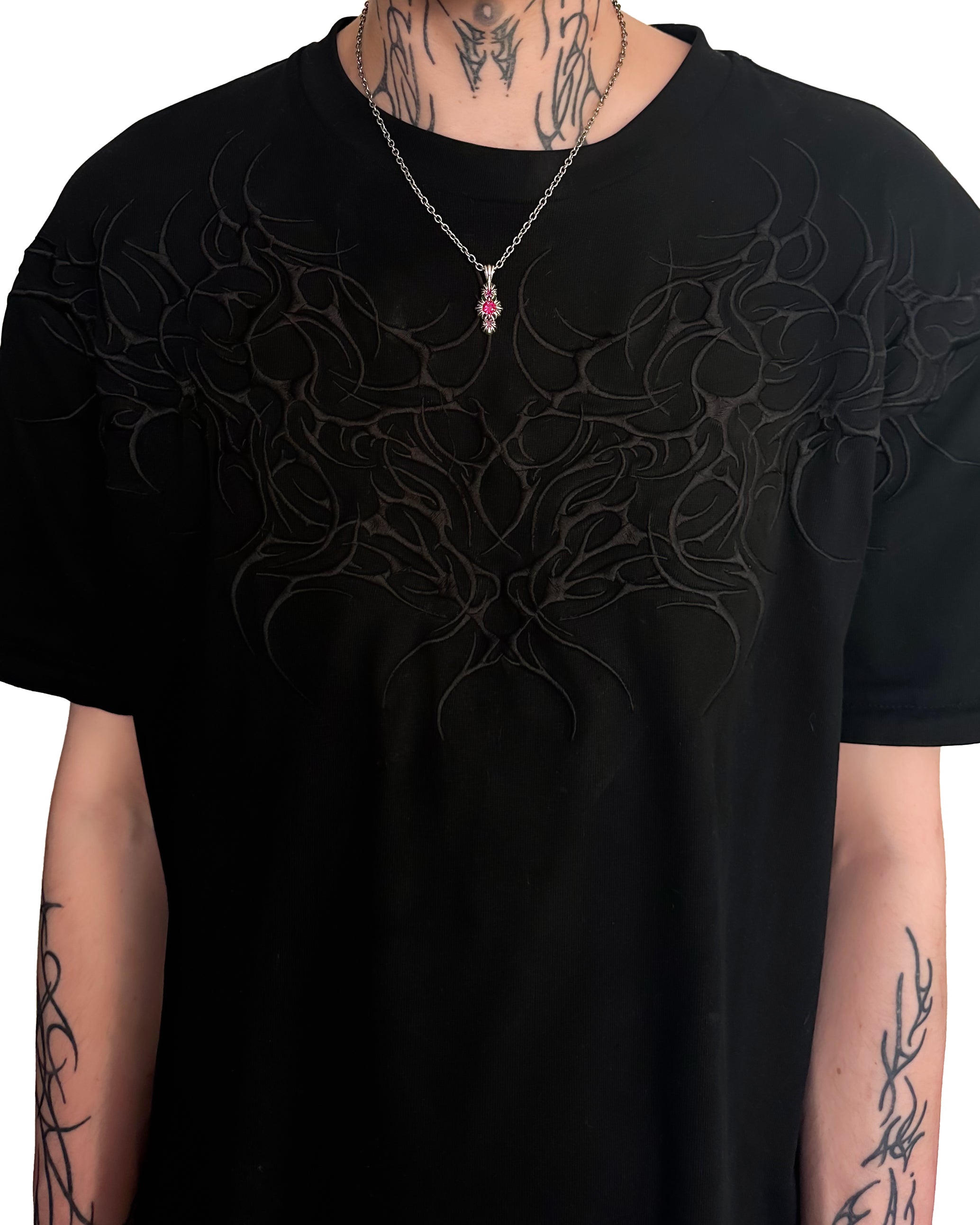 Black t-shirt with intricate design worn by a person with tattoos with red gemstone necklace.