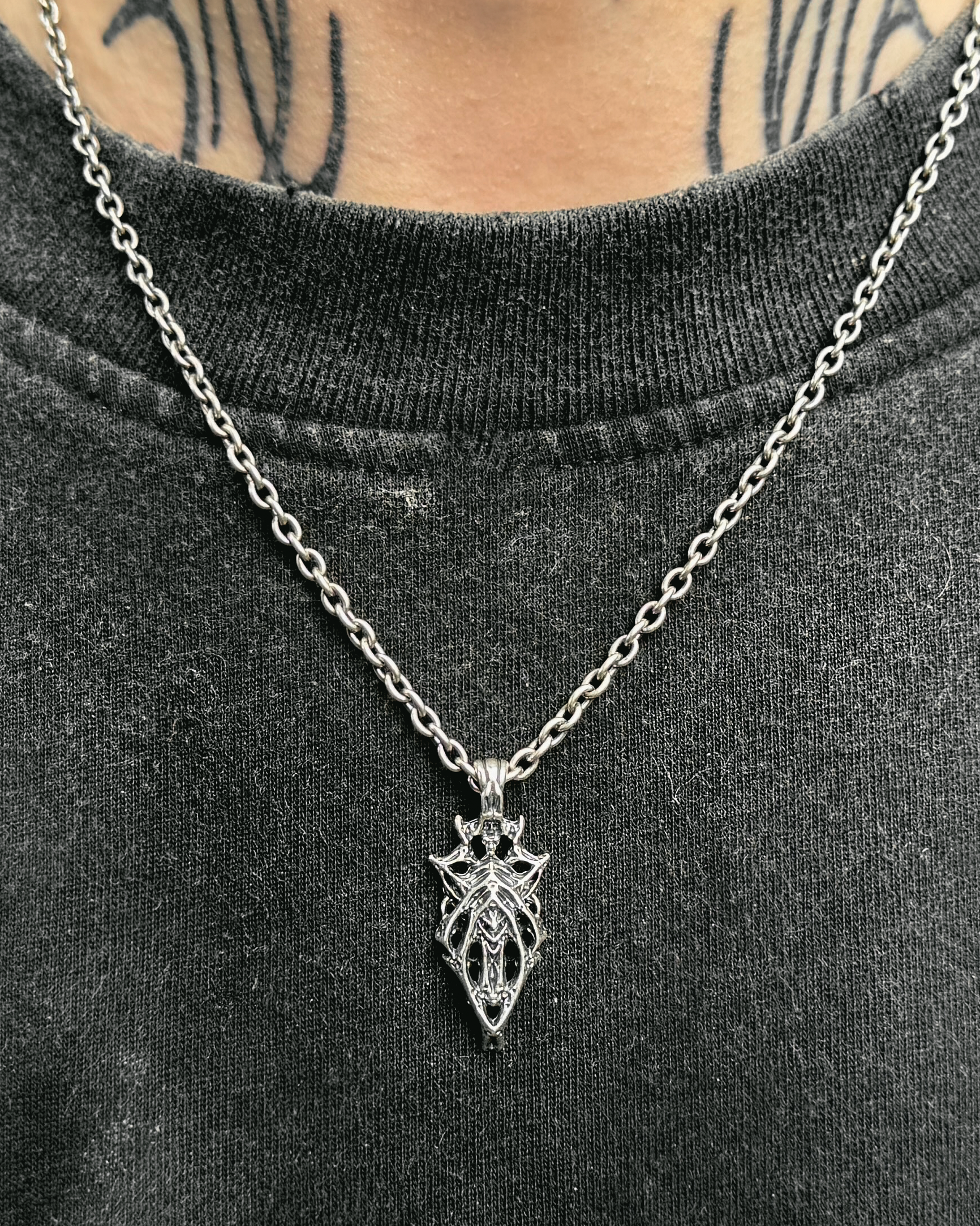 A sterling silver necklace with a geometric web-like pendant on a male subject.
