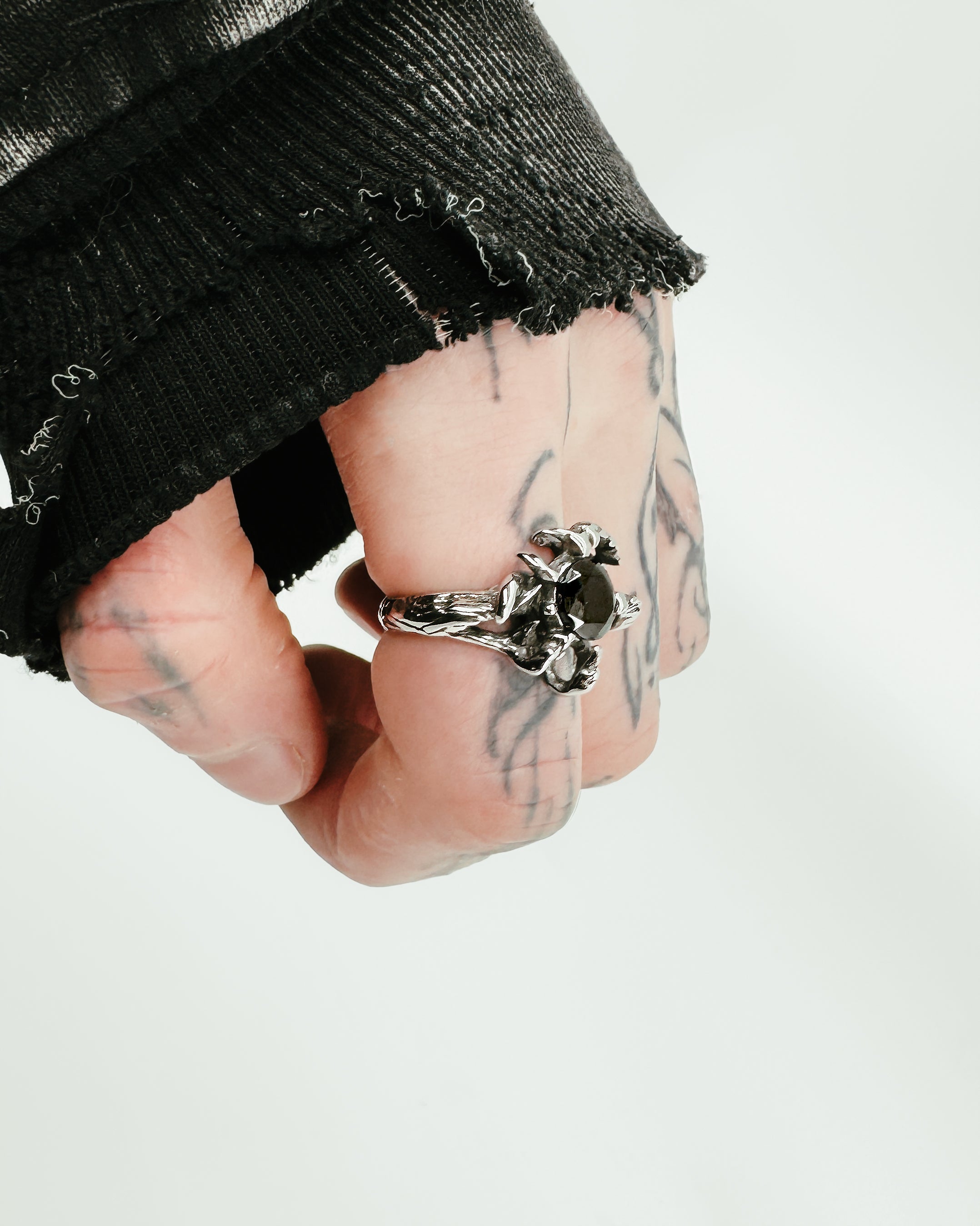 A sterling silver ring with a band designed as claw-like prongs holding a central onyx gemstone on a male's hand with tattoos.