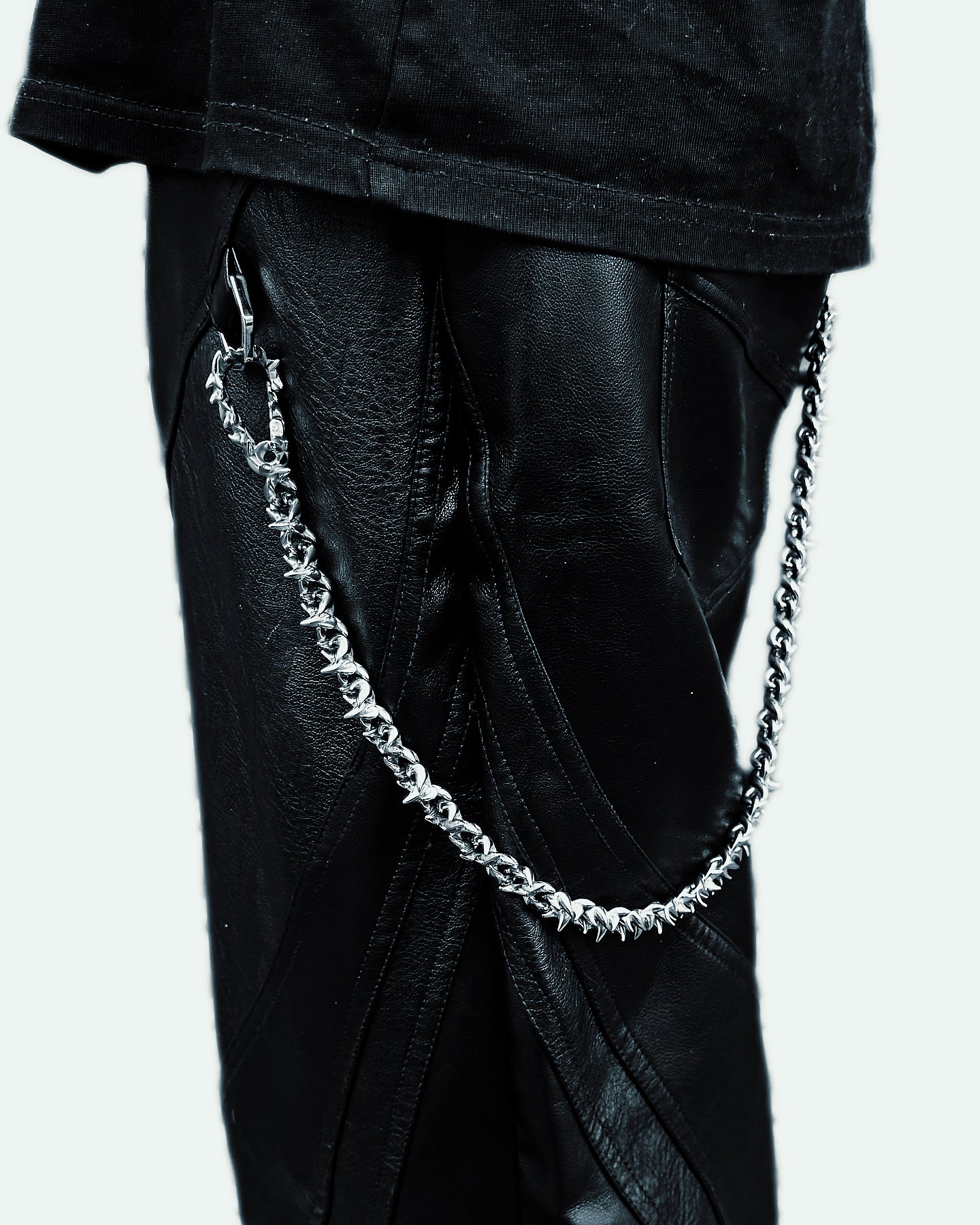 Close-up of a silver chain hanging from a pair of black leather pants