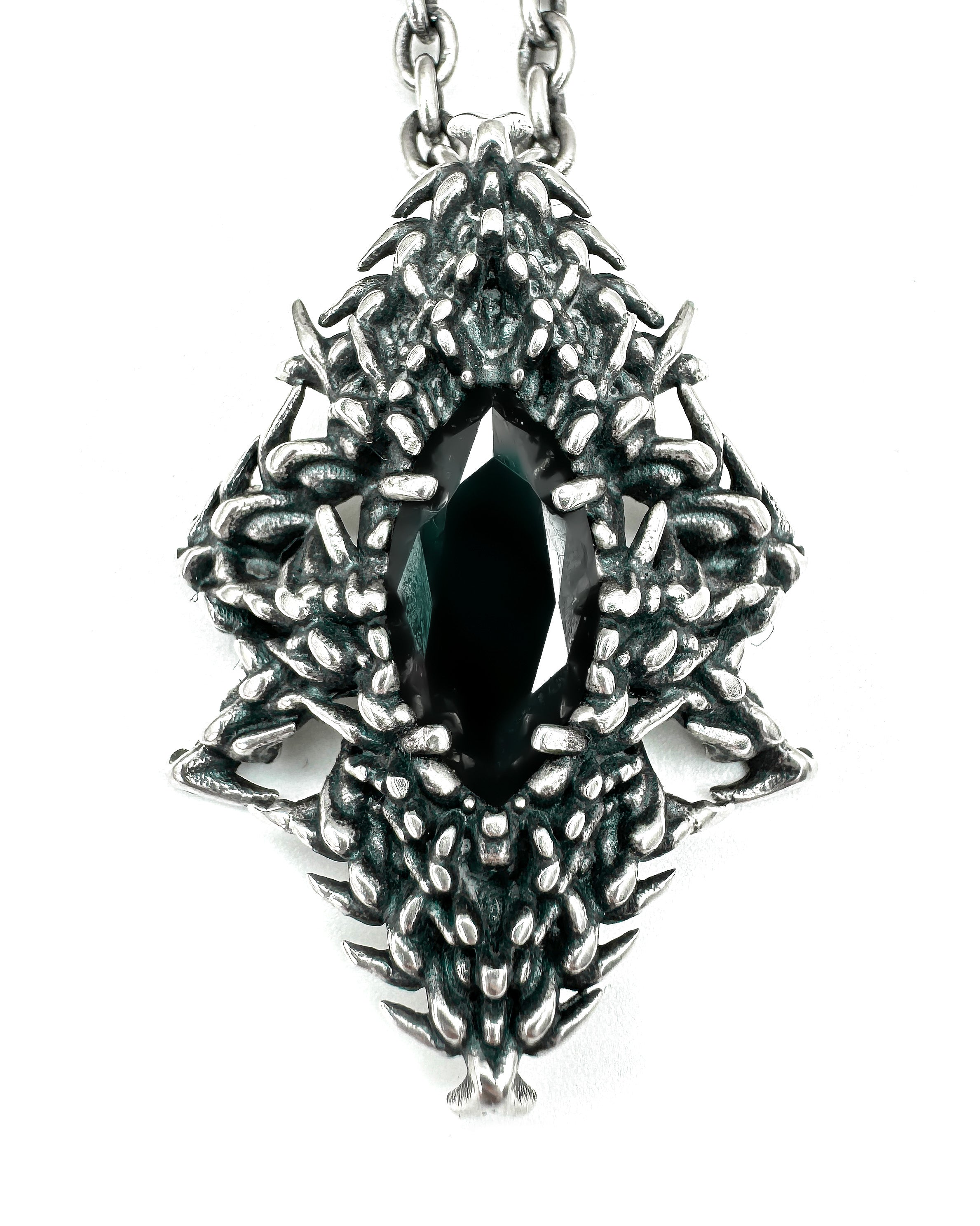A silver necklace featuring a claw-set black gemstone with intricate designs on the sides.