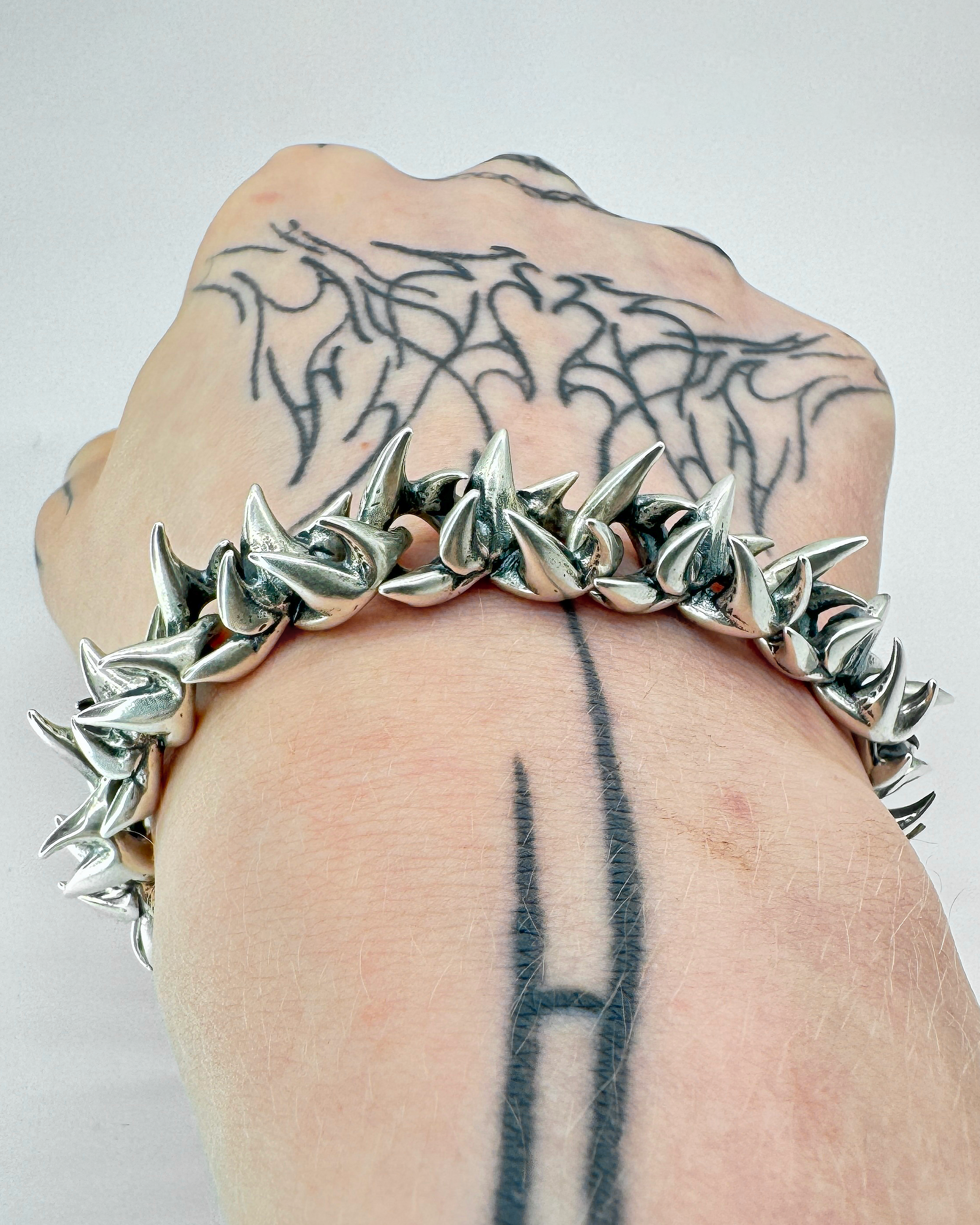 A bracelet with silver infinity links and a clasp, on a tattooed males wrist.