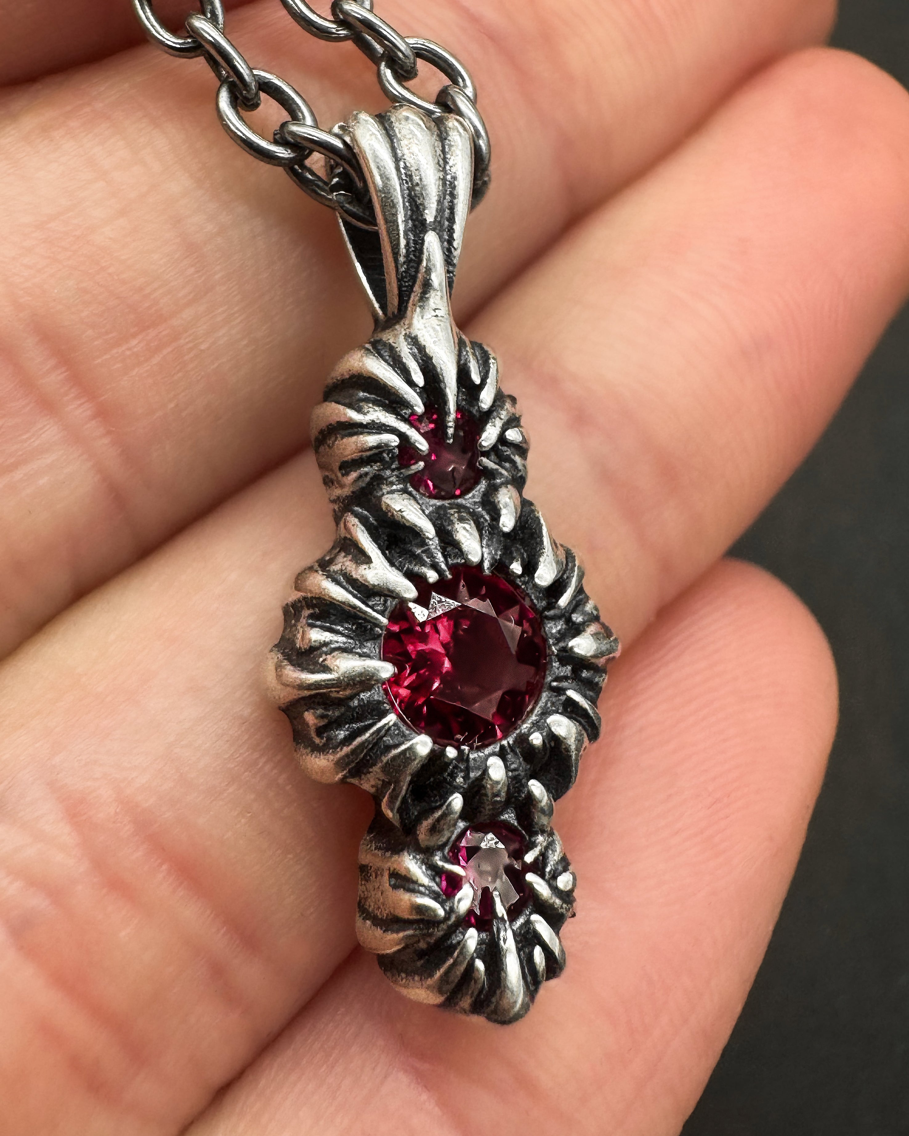 Silver pendant with a red gemstone held between fingers